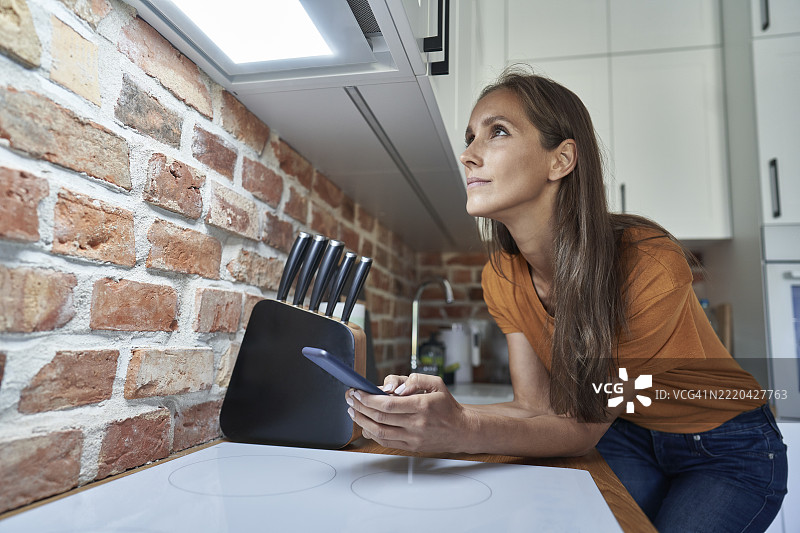 女人在家中靠着厨房台面，通过智能手机控制灯光图片素材