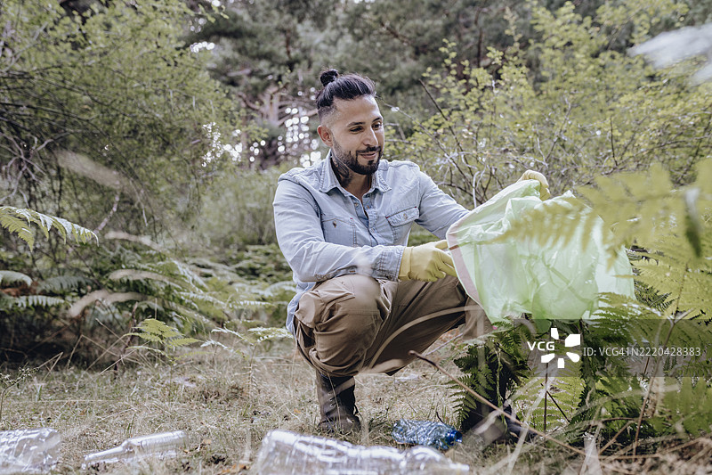 男性环保主义者蹲下身子在森林里用袋子收集塑料垃圾图片素材