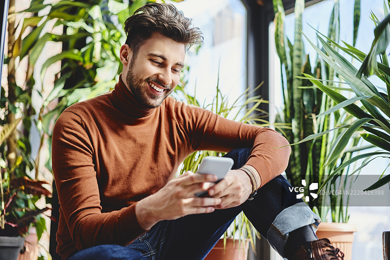 微笑的帅气男士在家窗边使用智能手机图片素材
