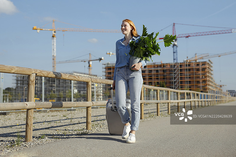 红发女性在建筑工地上提着植物和行李行走图片素材