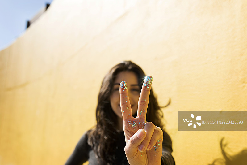 手指上沾有闪光粉的女性在墙前做出和平手势图片素材