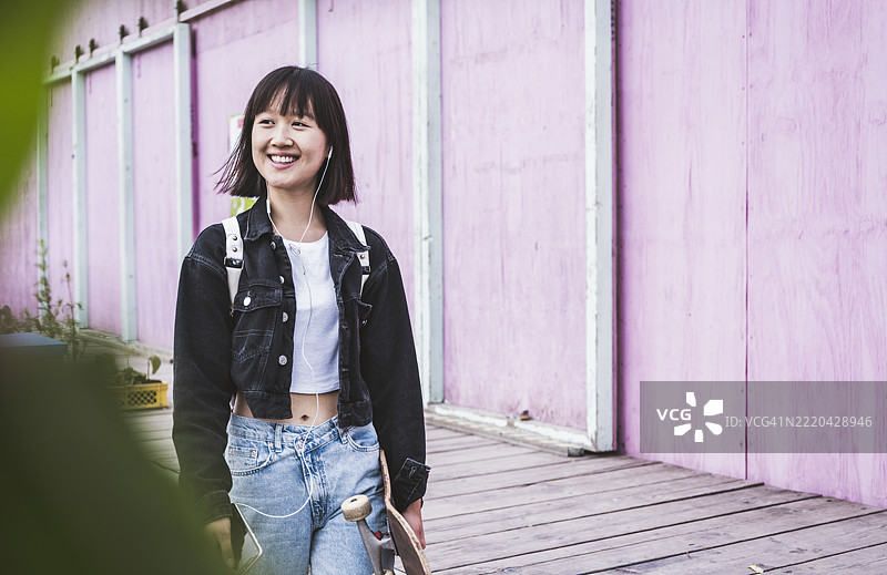 微笑的少女在人行道上推着滑板车图片素材