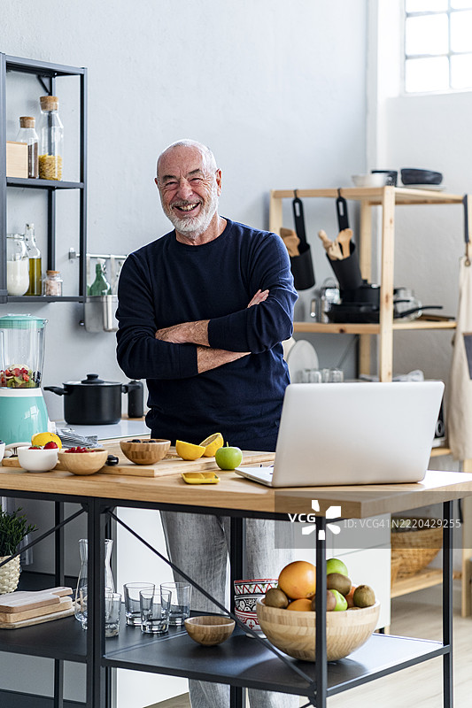 微笑的男人在厨房里双臂交叉站立图片素材