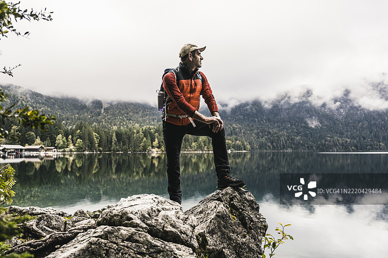 背包男站在岩石上看着湖泊图片素材