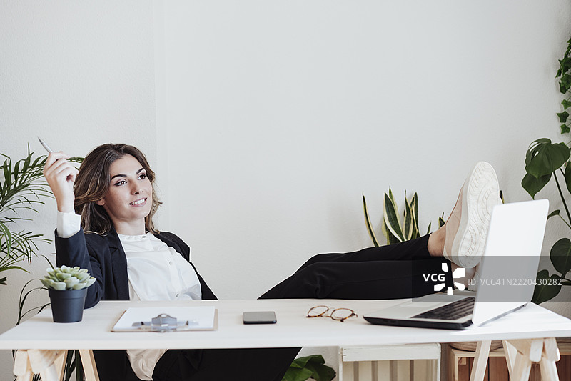 深思熟虑的女商人在办公室的桌子上翘起脚来坐着图片素材