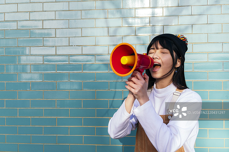 年轻女性在青绿色砖墙前通过扩音器大喊图片素材