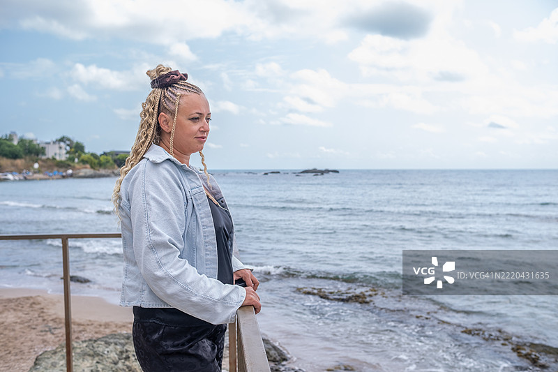 一位穿着黑色和浅色牛仔夹克的女性靠在桥的栏杆上。图片素材