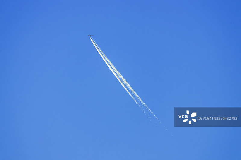 喷气式飞机在晴朗的蓝天中高飞，留下白色的凝结尾迹。图片素材