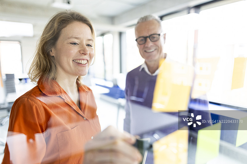 快乐的金发女商人在玻璃墙上写便签图片素材