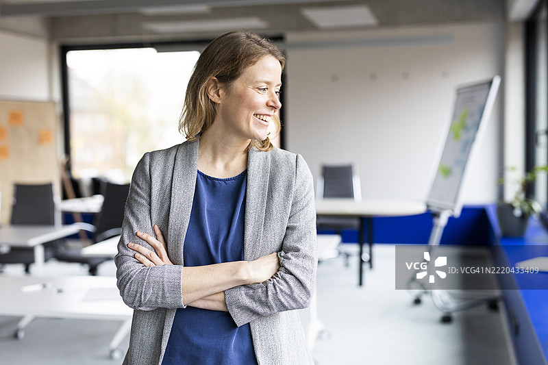 快乐的女商人在办公室里双臂交叉站立图片素材