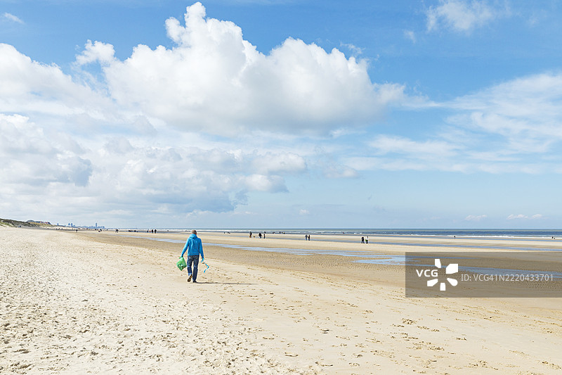 在比利时弗兰德地区的海滩上收集垃圾的男子图片素材