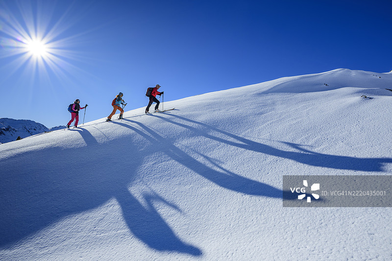 三个人在阳光明媚的冬日山中进行越野滑雪图片素材