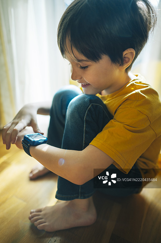 孩子坐在家里的地板上看着智能手表图片素材