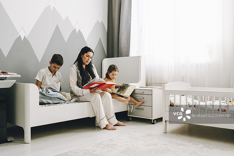 孕妈妈在温馨的卧室里和孩子们一起阅读图片素材