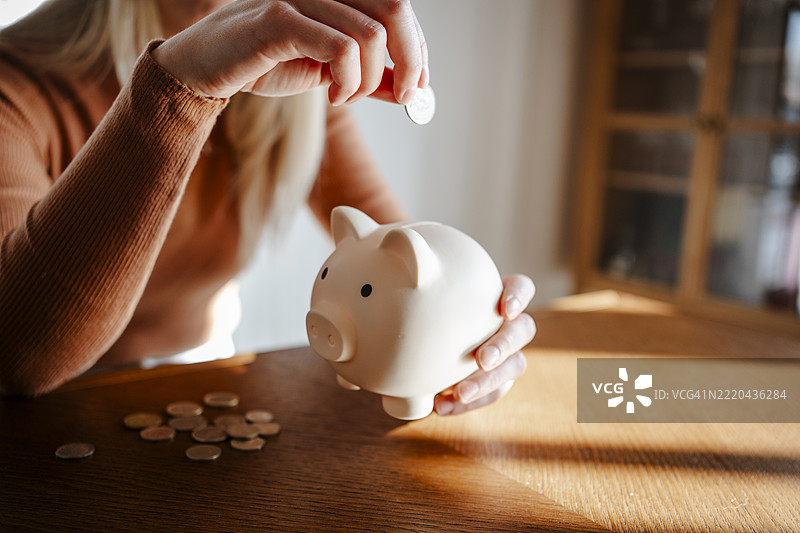 女人在室内的木桌上用储蓄罐存钱图片素材