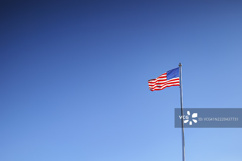在晴朗的蓝天背景下，国旗在旗杆上飘扬图片素材