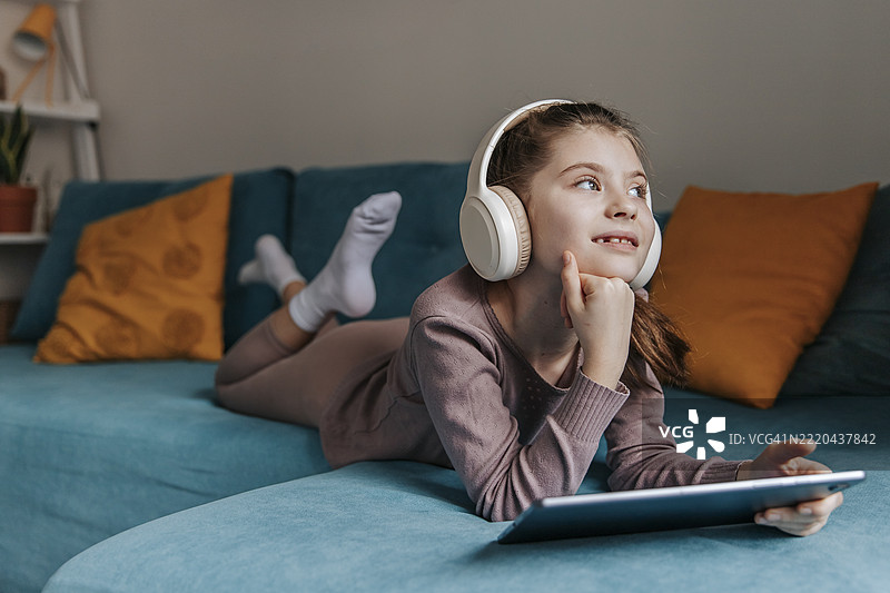 女孩在室内沙发上戴着耳机使用平板电脑图片素材