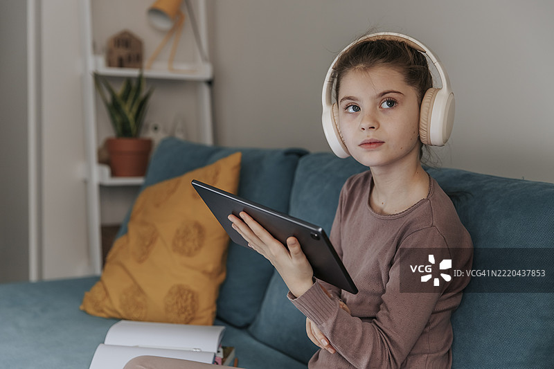 女孩在室内沙发上戴着耳机使用平板电脑图片素材