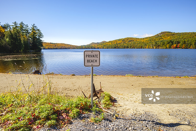 美国宁静湖泊旁的私人海滩标志，周围是秋季的树叶。图片素材