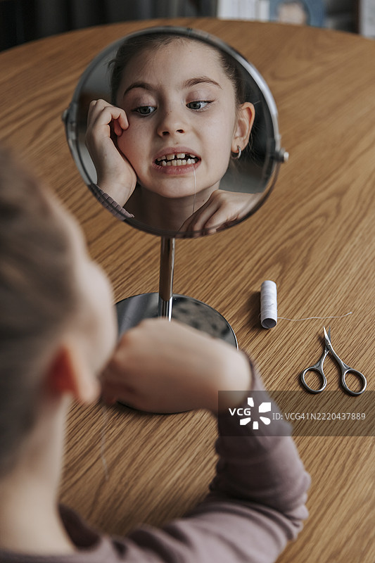 女孩在室内照镜子，仔细观察她的乳牙。图片素材