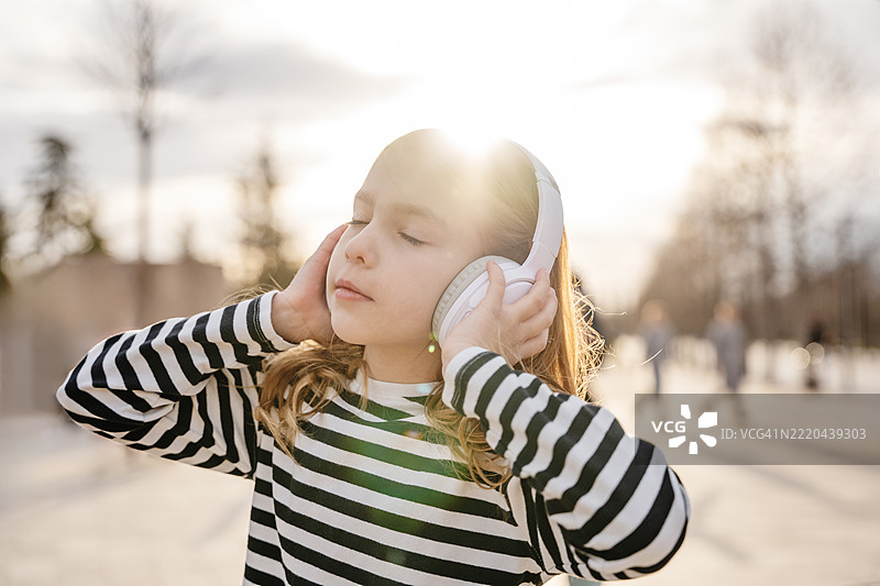 女孩在阳光明媚的公园里享受音乐，戴着耳机。图片素材