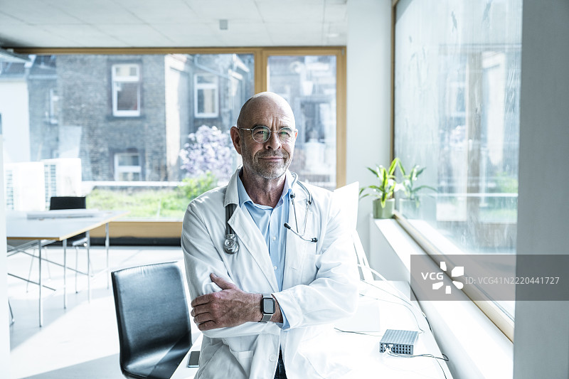 自信的医生站在明亮的诊所办公室里，双臂交叉。图片素材