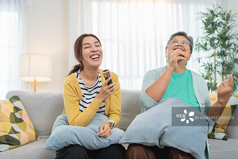 一位快乐的老年母亲和成年女儿在家中一起唱卡拉OK，欢声笑语。图片素材
