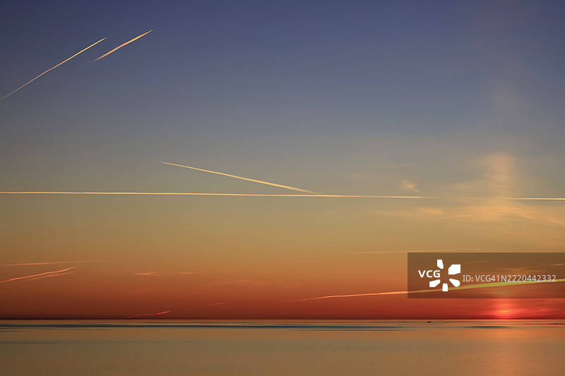 德国波罗的海上空的日落与天空中的飞机尾迹图片素材