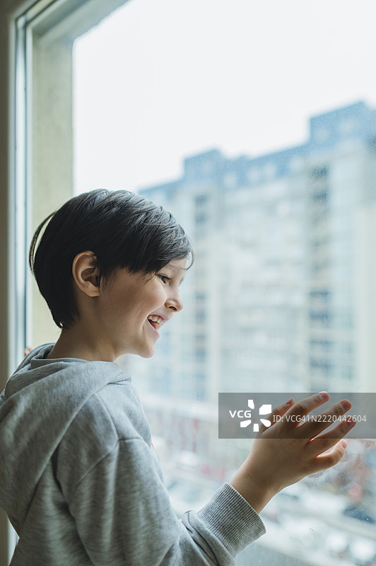 孩子在家隔离期间，微笑着从窗台向外望去图片素材