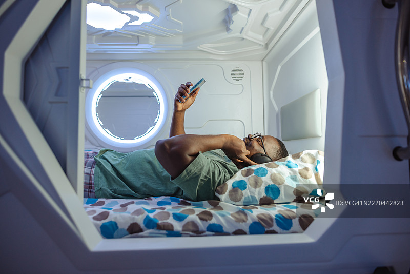 男子在未来主义胶囊中放松，戴着耳机，手持智能手机图片素材