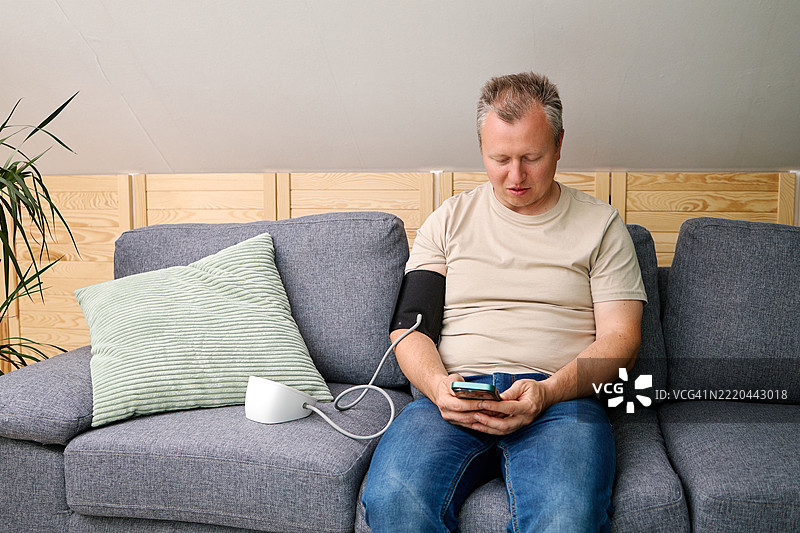 一名男子在家中使用血压计和测量袖带测量自己的血压。高血压和低血压的概念。在家自我检查。图片素材