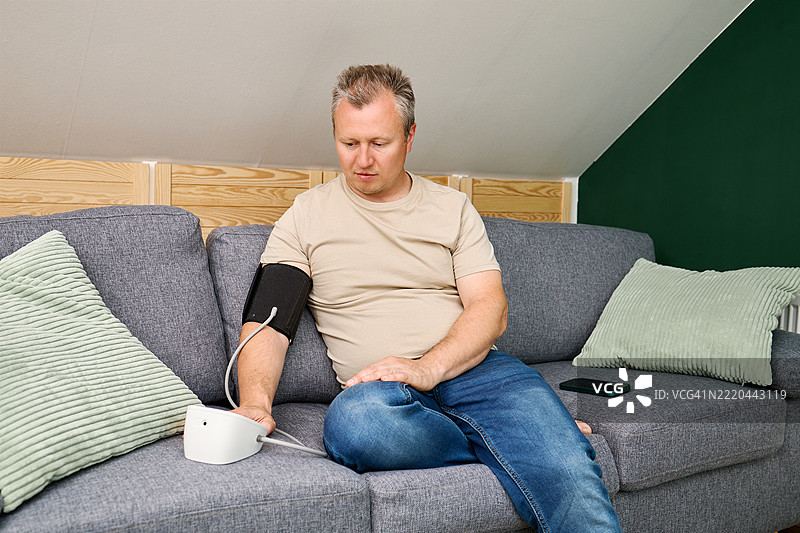 一名男子在家中使用血压计和测量袖带测量自己的血压。高血压和低血压的概念。在家自我检查。图片素材
