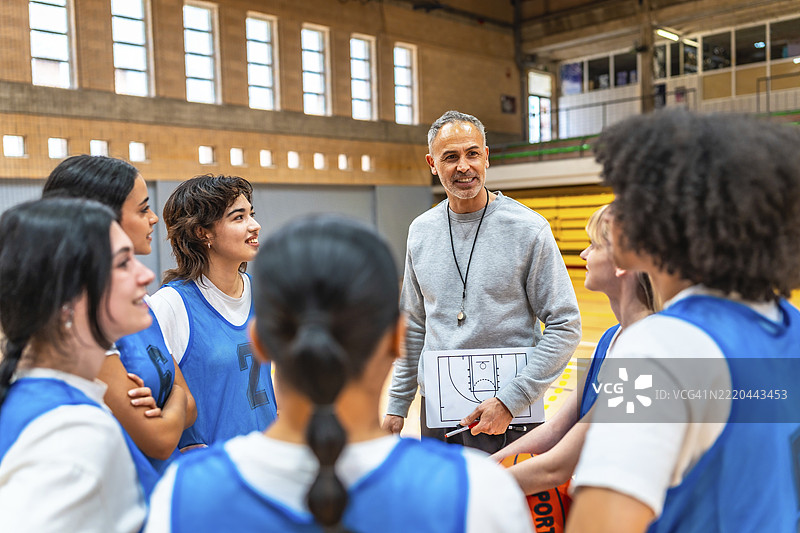 篮球教练手持战术板，在体育馆里向一群女运动员讲解比赛策略图片素材