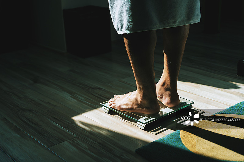 在阳光明媚的家中称体重的人图片素材