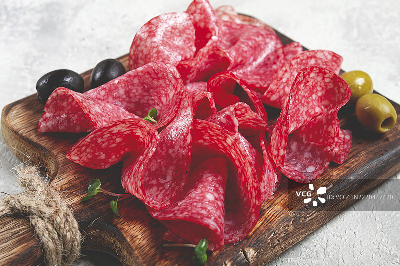 切片的萨拉米香肠，放在木砧板上，装饰着橄榄和香草，特写，无人。图片素材