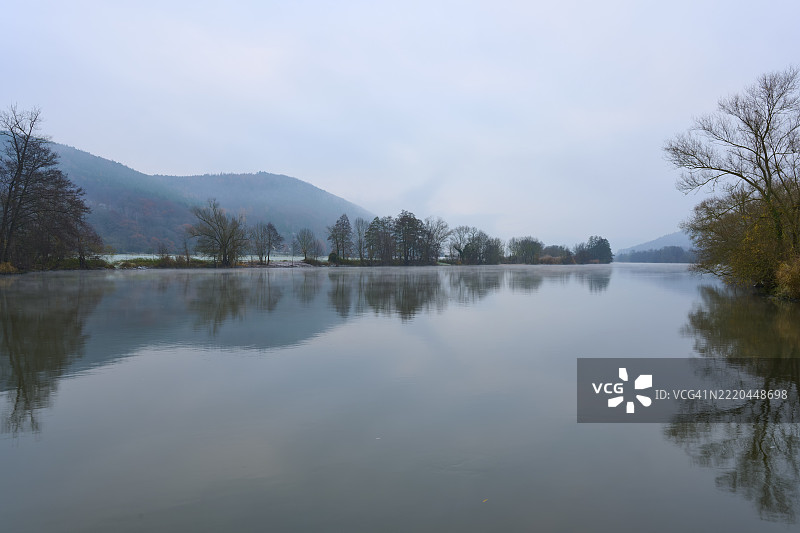 宁静的河流上空雾气弥漫，远处是山丘和树木，地点：德国巴伐利亚州劳登巴赫，梅因，斯佩萨特，奥登瓦尔德。图片素材