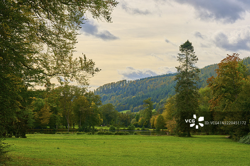 德国巴伐利亚州奥登瓦尔德阿莫尔巴赫的秋季风景，绿草如茵，高大的树木和多云的天空。图片素材