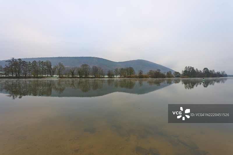 宽广的河流，平静的水面，背景是群山，阴云密布，位于德国巴伐利亚的劳登巴赫，梅因，斯佩萨特，奥登瓦尔德。图片素材