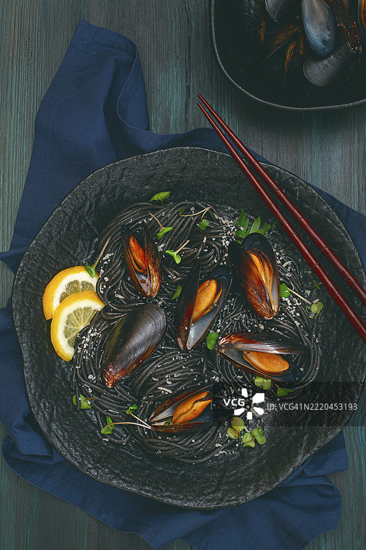 黑色鱿鱼意大利面，黑色意大利面，配有煮熟的贻贝，放在黑色盘子上，撒上香菜和帕尔马干酪，特写，选择性对焦，无人。图片素材