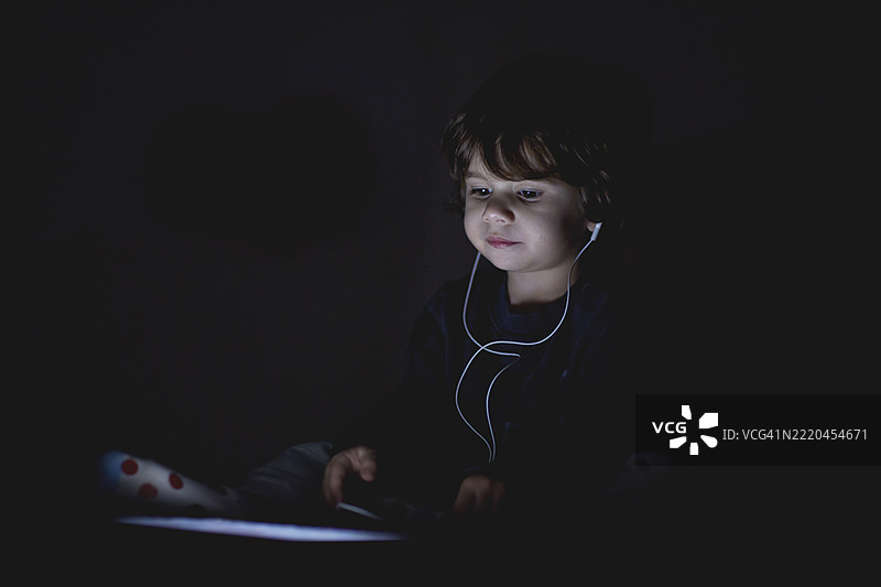 孩子在昏暗的灯光下安静地享受使用设备的时光图片素材