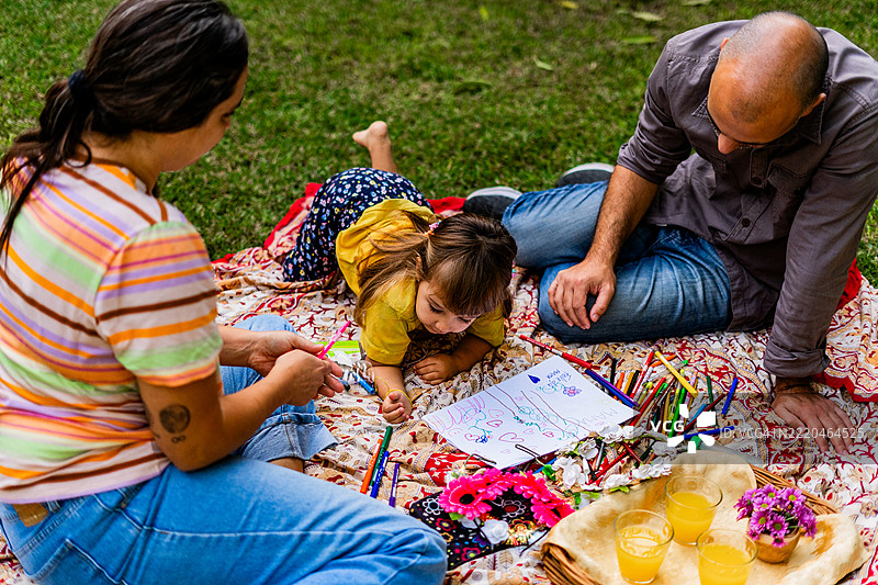 小女孩在家里准备母亲节贺卡，父母在旁协助。图片素材