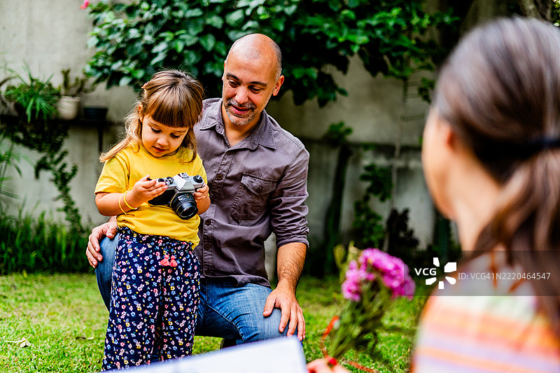 小女孩在家后院里在父亲的帮助下给母亲拍照图片素材