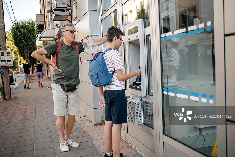 父亲和他的青少年儿子站在自动取款机前图片素材