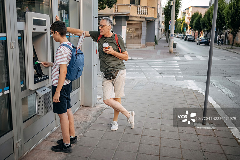 父亲和他的青少年儿子站在自动取款机前图片素材