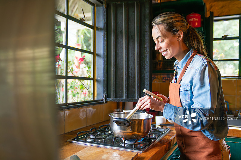 快乐的女人在木屋里做汤并微笑图片素材
