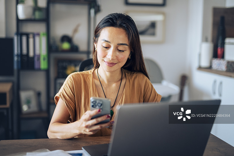 亚洲女性在家中使用移动设备远程工作。图片素材