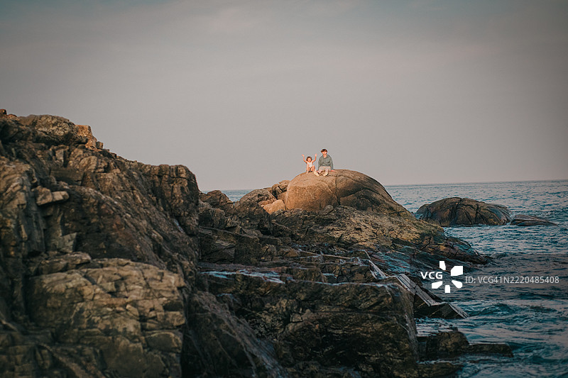 崎岖的海岸线，两名孩子坐在远处的岩石上图片素材