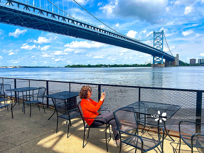 在费城本杰明·富兰克林大桥附近的樱桃街码头，一位女性正在放松并拍照。图片素材