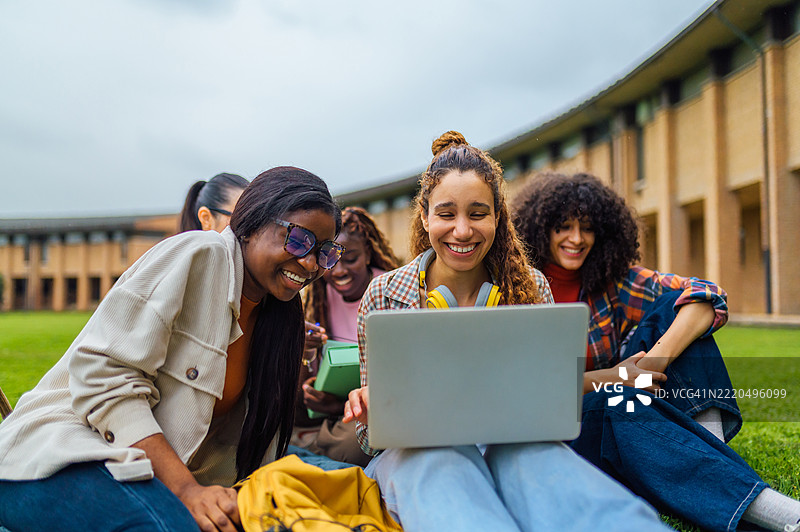 快乐的大学生在校园草坪上观看笔记本电脑图片素材