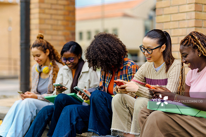 多种族女性学生在大学校园使用智能手机图片素材